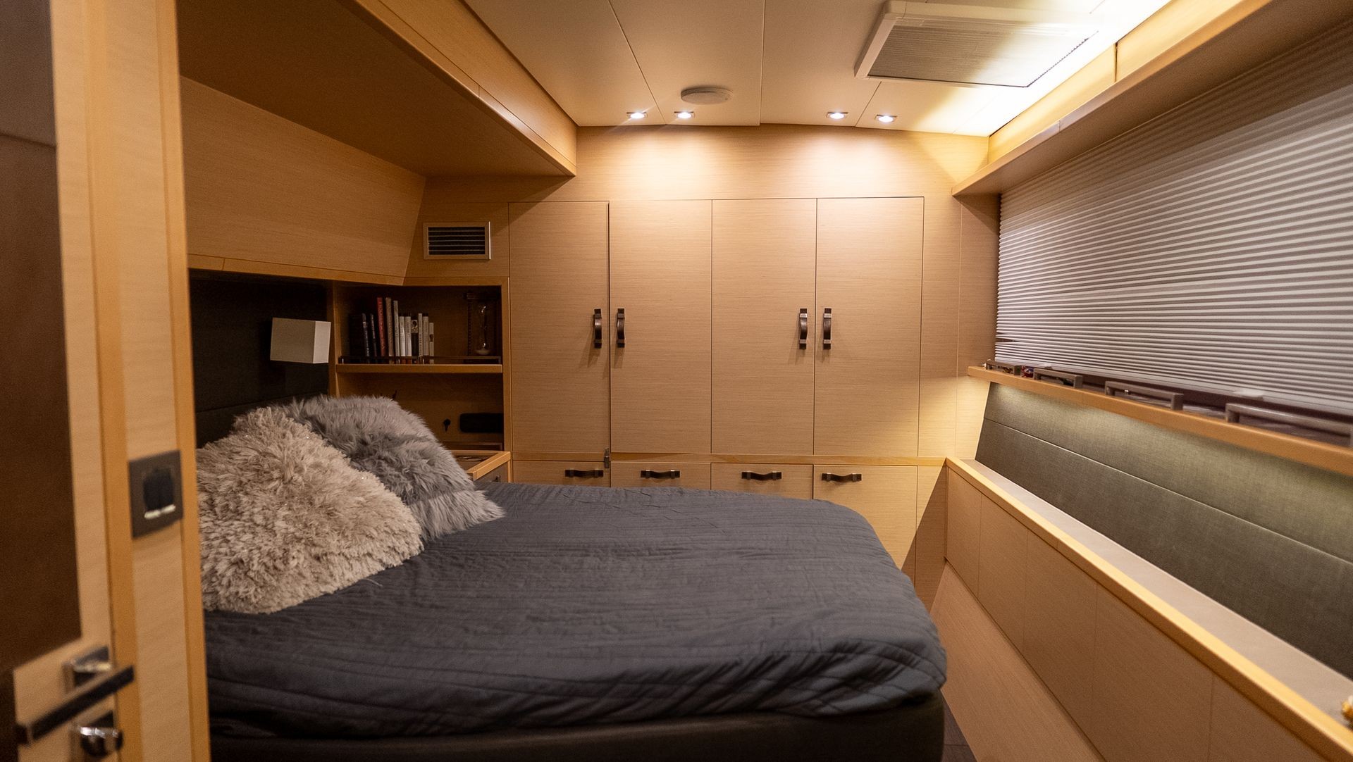 Cozy yacht cabin with a bed, soft pillows, built-in shelves, and warm lighting.