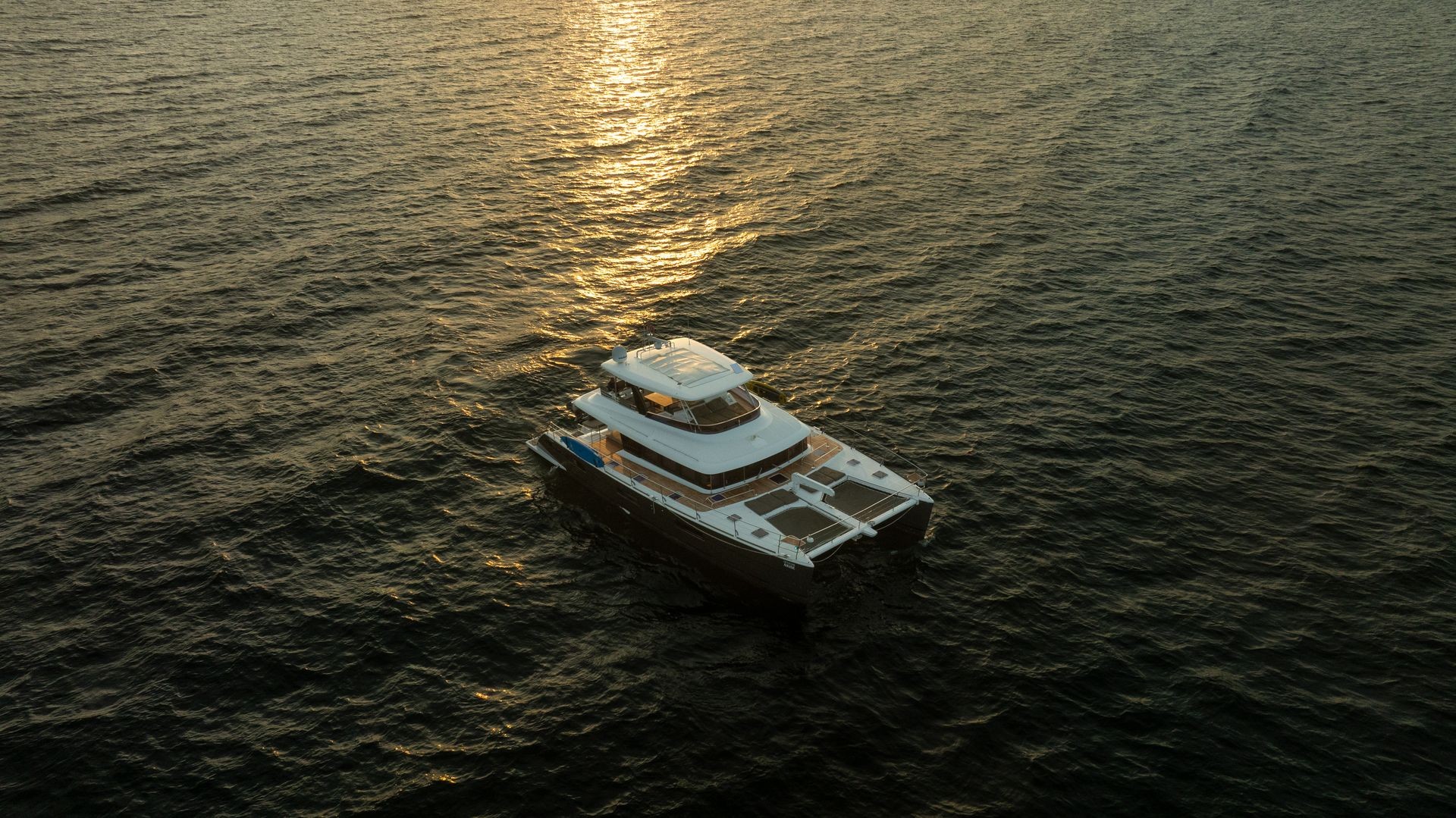Aerial view of a yacht navigating calm waters with sunset reflections on the sea surface.