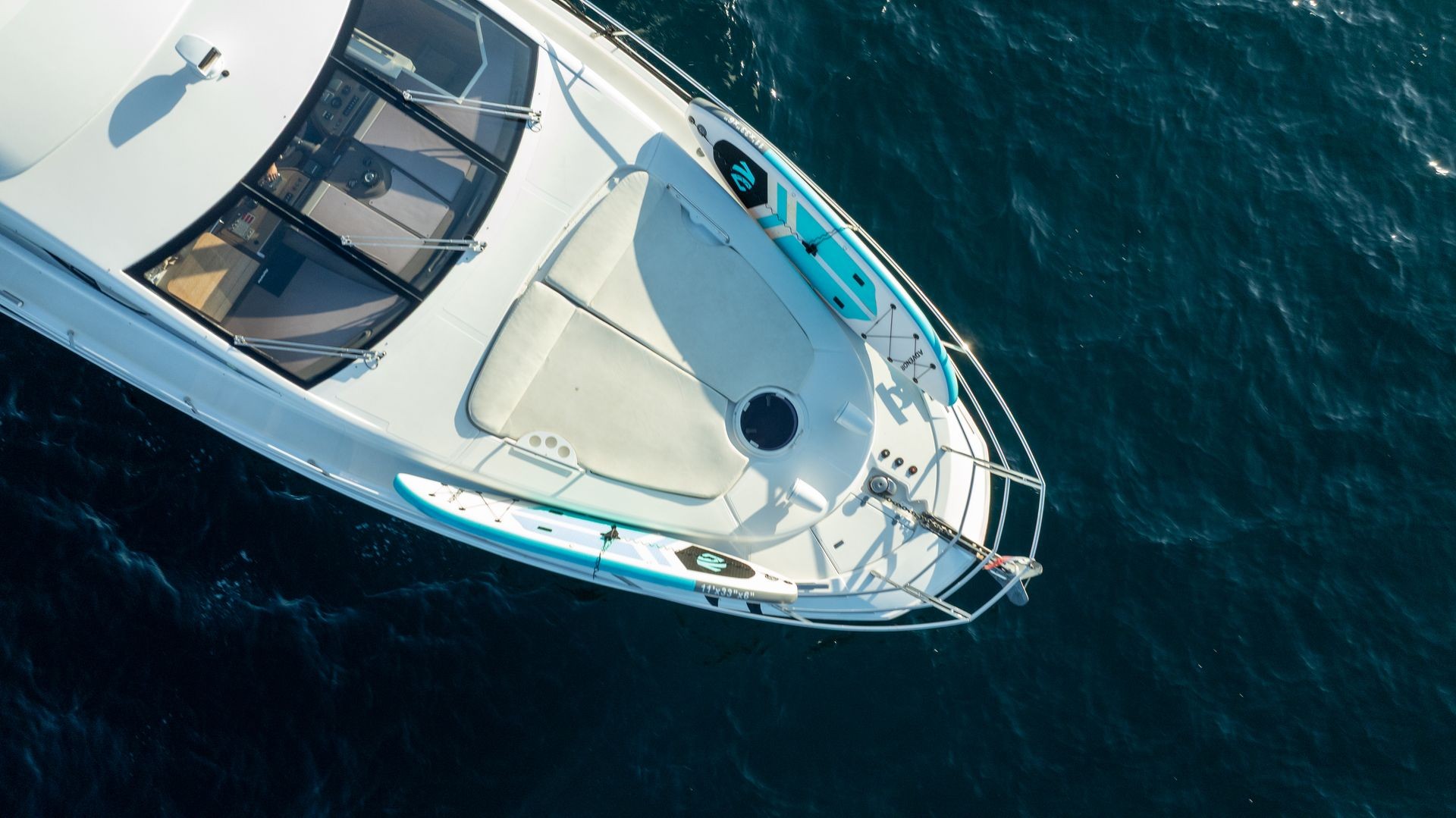 Aerial view of a yacht on blue water, with sun deck and attached surfboard visible.