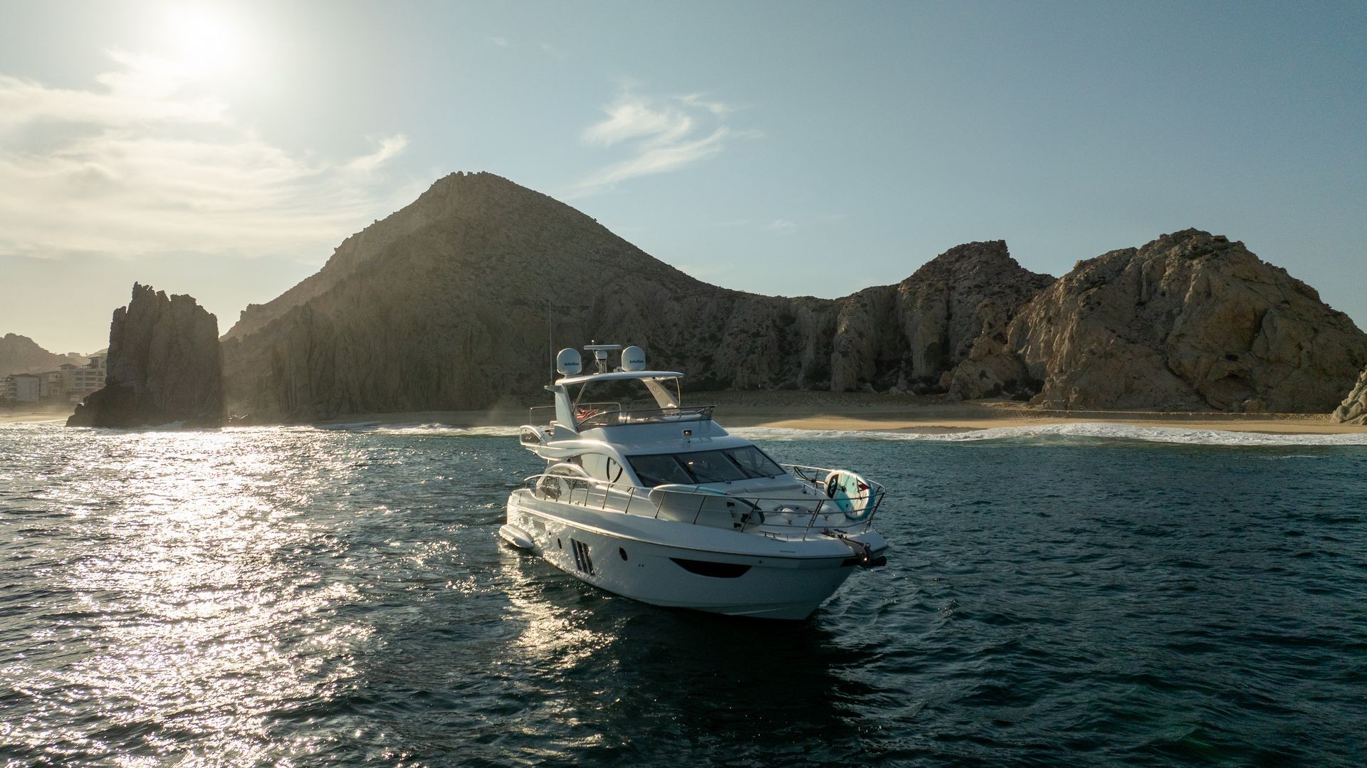 Luxury yacht sailing near rocky cliffs and sandy beach under a clear sky.