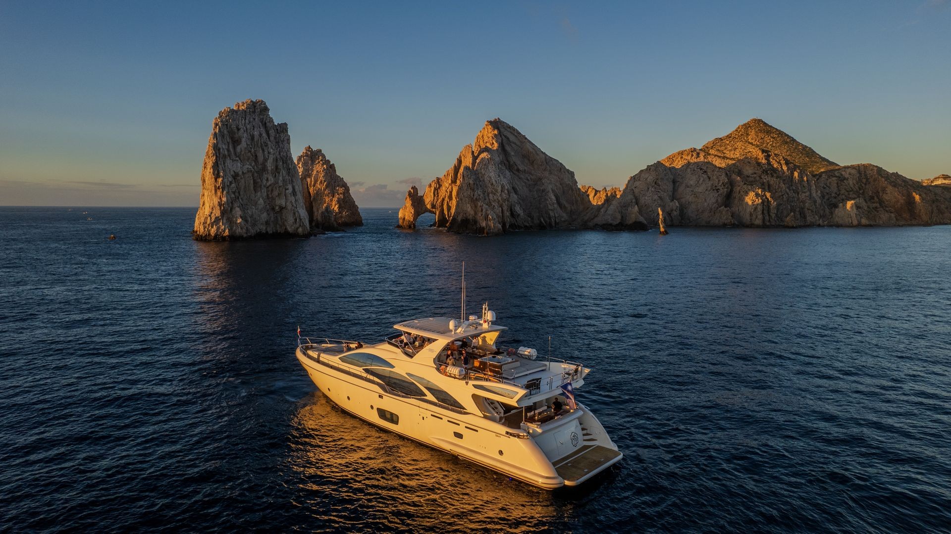 Luxury yacht sailing near rock formations at sunset in Cabo San Lucas, Mexico.
