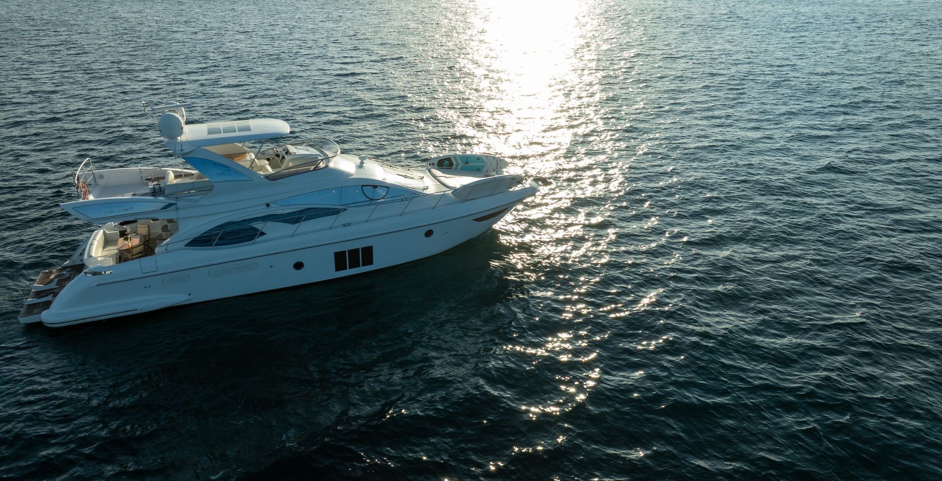 Luxury yacht floating on calm ocean waters with sunlight reflecting off the surface.