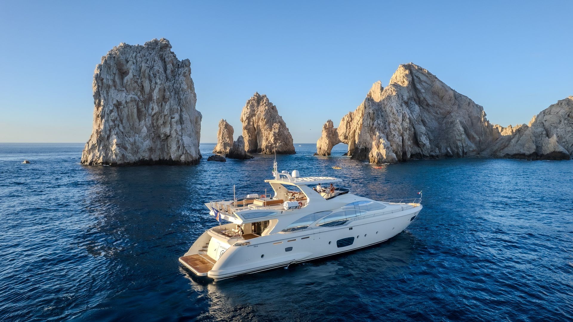 Luxury yacht sailing near large rock formations in a calm blue sea under a clear sky.