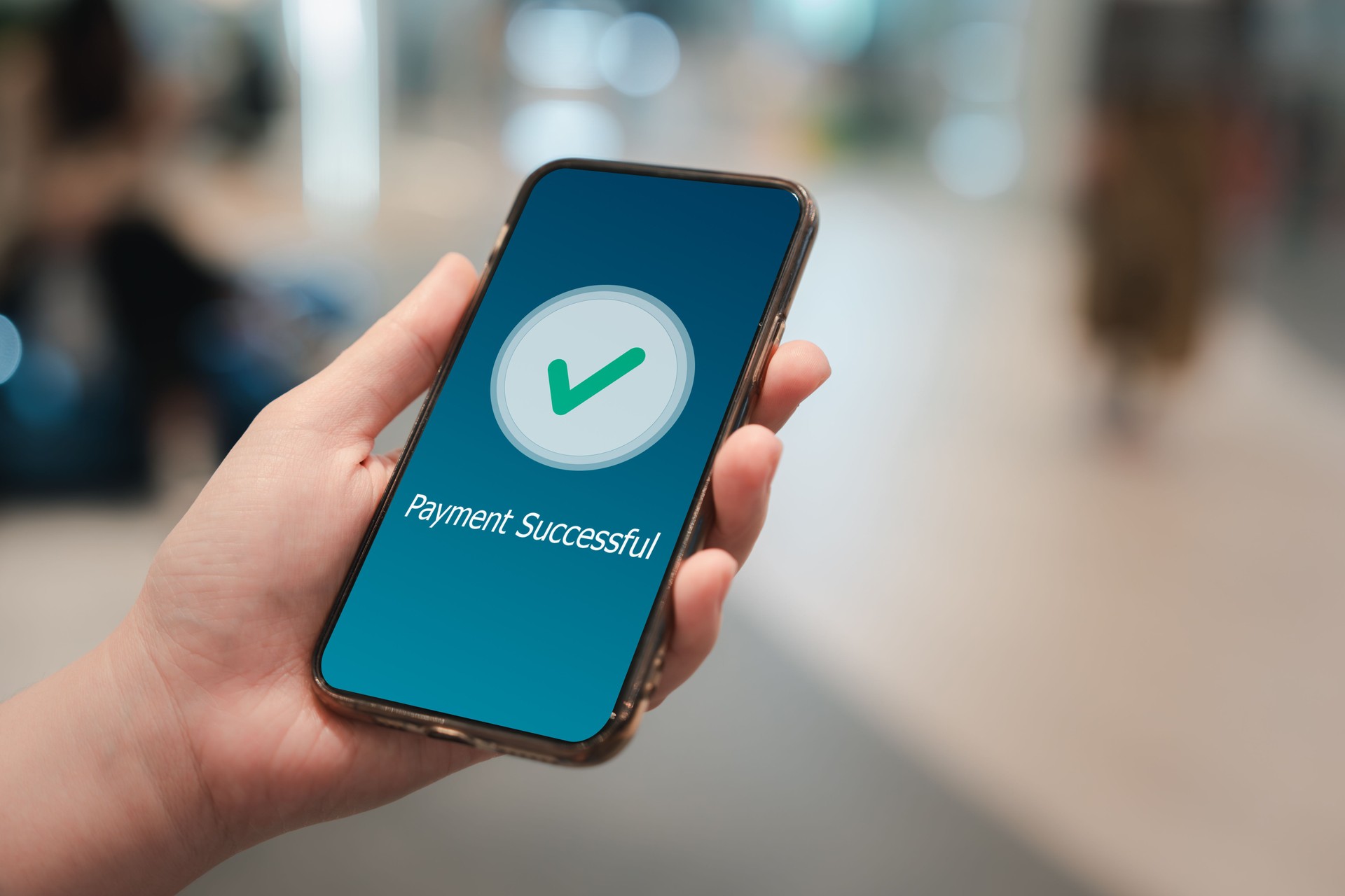 Hand holding mobile phone and application showing payment successful message with green check mark.